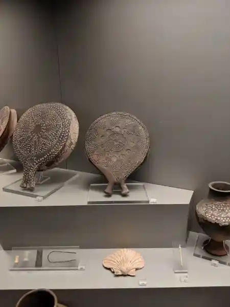 Museum display of Early Cycladic II period grave offerings including decorated ceramic frying pans from Chalandriani, Syros, 2800-2300